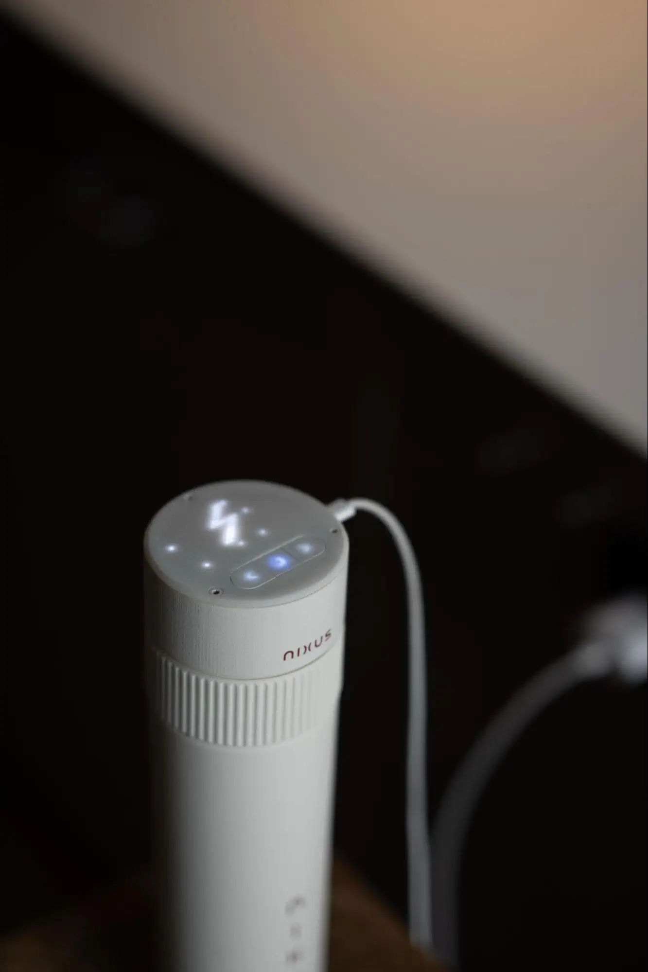 Close-up of the top of the white canister charging via cable, showing a glowing LED lightning bolt icon and control buttons.